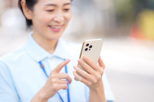 屋外でスマートフォンを使う笑顔の女性介護士